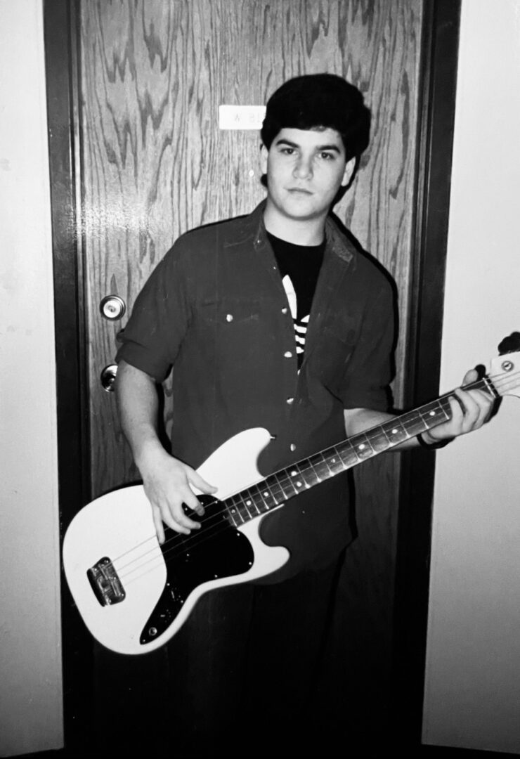 A young man holding a guitar in front of a door.